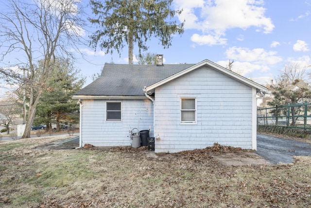 rear view of house featuring a shingled roof, a chimney, and fence