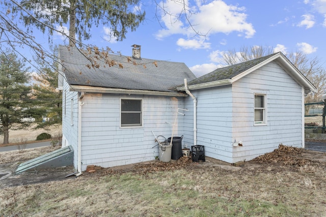 back of house with roof with shingles and a chimney