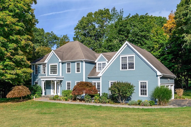 colonial home featuring a garage, a front yard, and roof with shingles