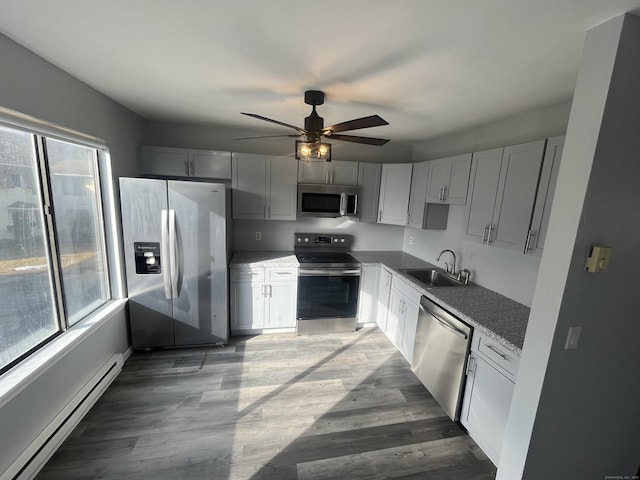 kitchen featuring ceiling fan, appliances with stainless steel finishes, baseboard heating, light wood-style floors, and a sink