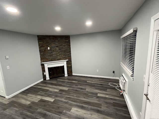 unfurnished living room featuring dark wood-style flooring, a wall unit AC, recessed lighting, a large fireplace, and baseboards