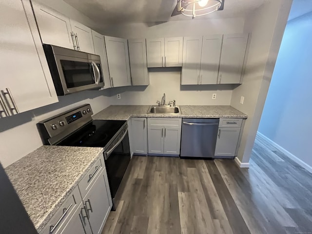 kitchen with light stone counters, stainless steel appliances, dark wood-type flooring, a sink, and baseboards