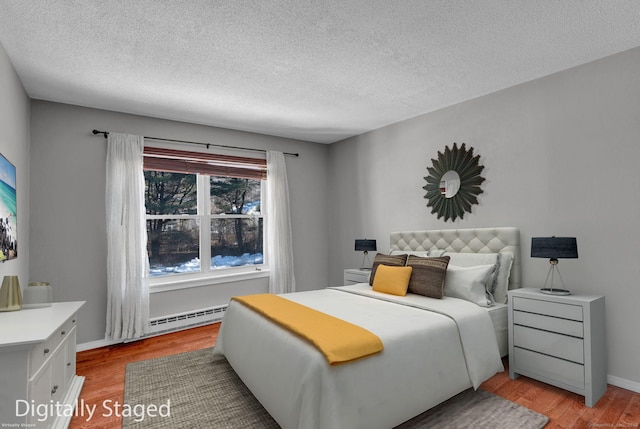 bedroom featuring a baseboard heating unit, baseboards, a textured ceiling, and light wood finished floors