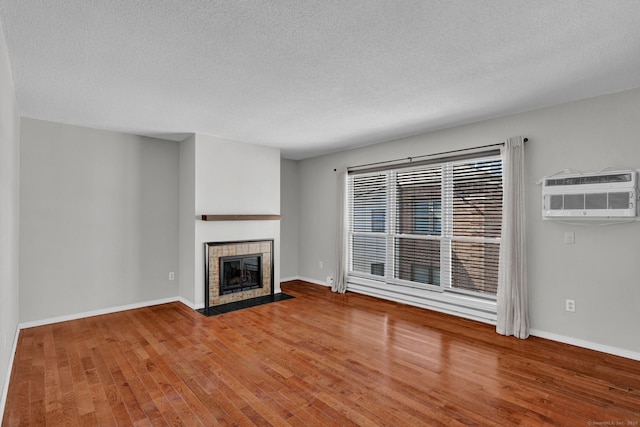 unfurnished living room with hardwood / wood-style flooring, a fireplace, baseboards, and a wall mounted AC