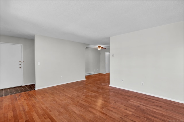 empty room with a textured ceiling, a baseboard heating unit, wood finished floors, a ceiling fan, and baseboards