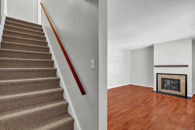 staircase with a textured ceiling, a fireplace, baseboards, and wood finished floors