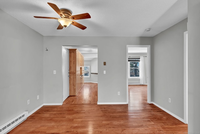 empty room with a baseboard radiator, light wood-style flooring, ceiling fan, a textured ceiling, and baseboards