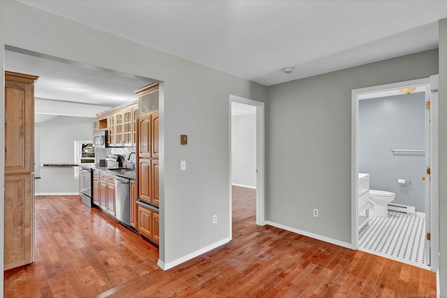 kitchen featuring a sink, appliances with stainless steel finishes, baseboard heating, light wood-type flooring, and dark countertops