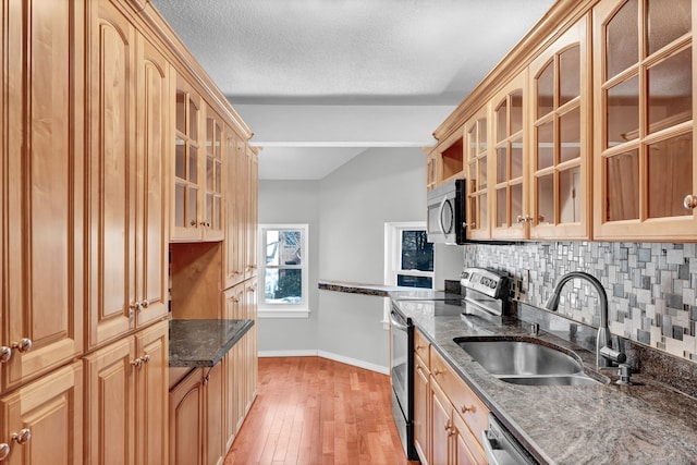 kitchen with stainless steel appliances, a sink, decorative backsplash, dark stone counters, and light wood finished floors