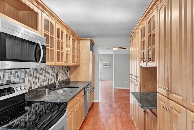 kitchen with ceiling fan, stainless steel appliances, a sink, light wood-style floors, and glass insert cabinets