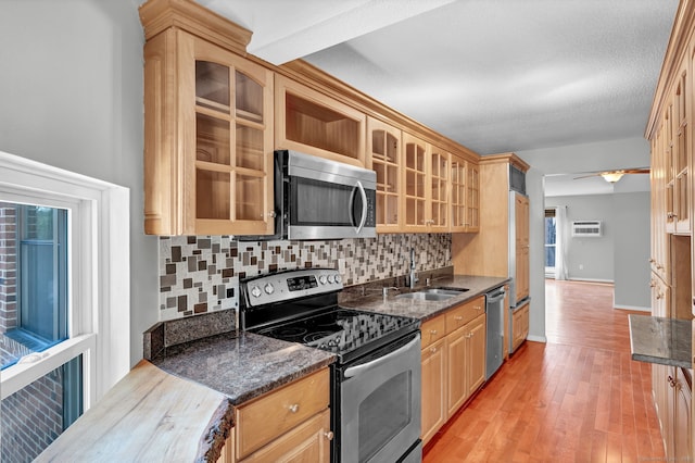 kitchen with stainless steel appliances, tasteful backsplash, glass insert cabinets, a sink, and light wood-type flooring