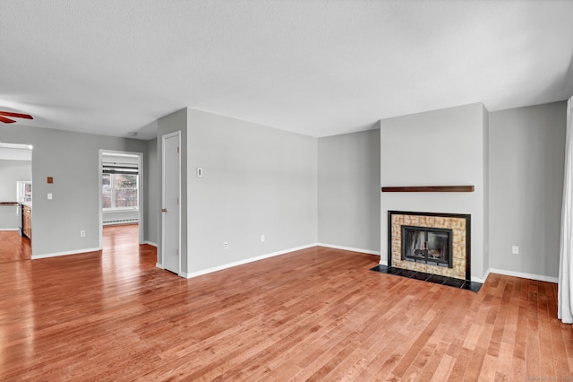 unfurnished living room with light wood finished floors, ceiling fan, baseboards, and a tiled fireplace