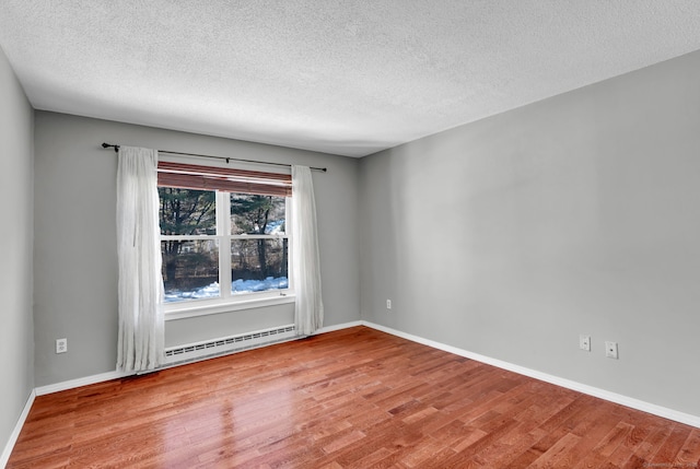 spare room with a baseboard heating unit, a textured ceiling, baseboards, and wood finished floors