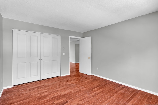 unfurnished bedroom featuring a textured ceiling, a closet, baseboards, and wood finished floors