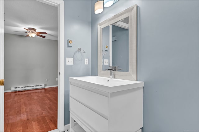 bathroom with baseboards, a ceiling fan, wood finished floors, baseboard heating, and vanity