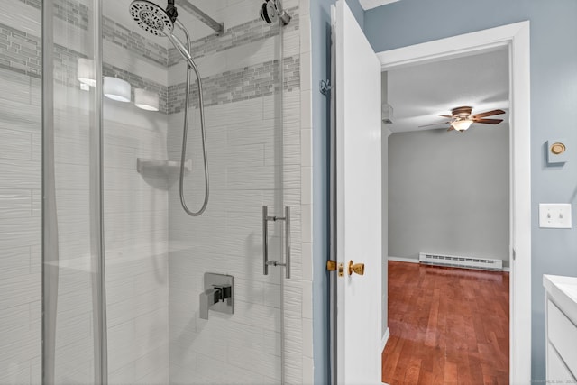 bathroom featuring a baseboard heating unit, ceiling fan, a shower stall, vanity, and wood finished floors