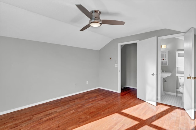 unfurnished bedroom featuring lofted ceiling, wood finished floors, a ceiling fan, baseboards, and ensuite bath