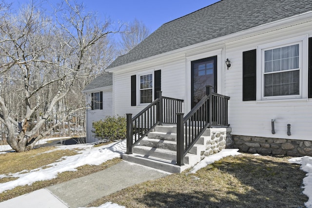 snow covered property entrance featuring a shingled roof