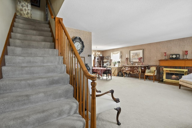 staircase with a chandelier, a textured ceiling, carpet flooring, and a fireplace with flush hearth