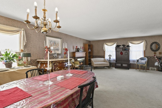 carpeted dining space with a textured ceiling, wallpapered walls, visible vents, and an inviting chandelier