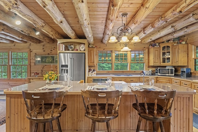 kitchen with a kitchen island with sink, wood walls, beam ceiling, and stainless steel fridge with ice dispenser