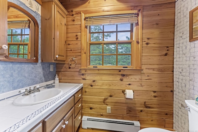 bathroom with a baseboard radiator, wood walls, vanity, and toilet