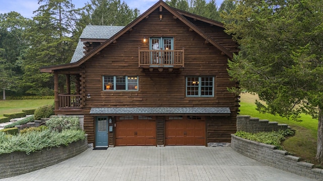 log-style house featuring a garage, log exterior, decorative driveway, and a balcony