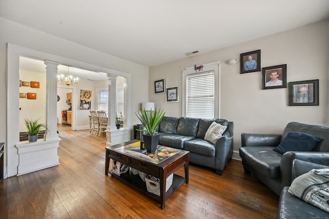 living area featuring a wealth of natural light, decorative columns, visible vents, and hardwood / wood-style flooring