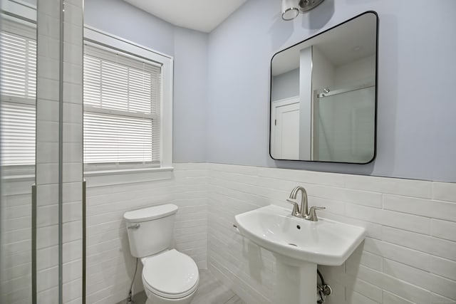 bathroom with a sink, toilet, tile walls, and wainscoting