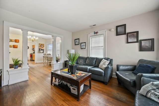 living room with baseboards, visible vents, ornate columns, an inviting chandelier, and wood-type flooring