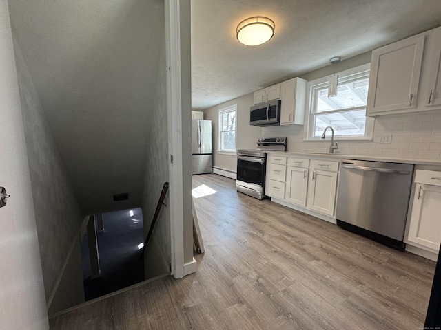 kitchen with backsplash, appliances with stainless steel finishes, light wood-type flooring, and a sink