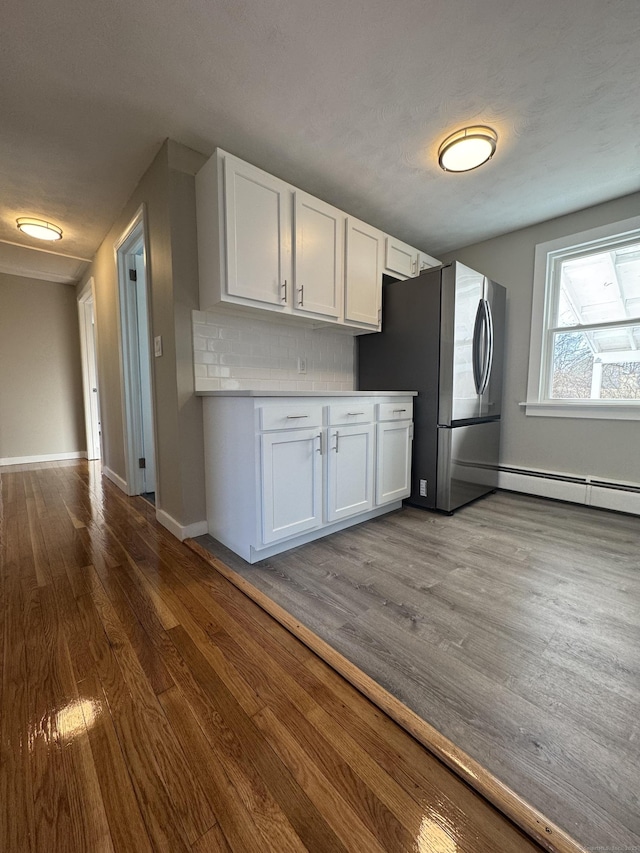 kitchen with backsplash, dark wood-style floors, freestanding refrigerator, white cabinetry, and baseboards