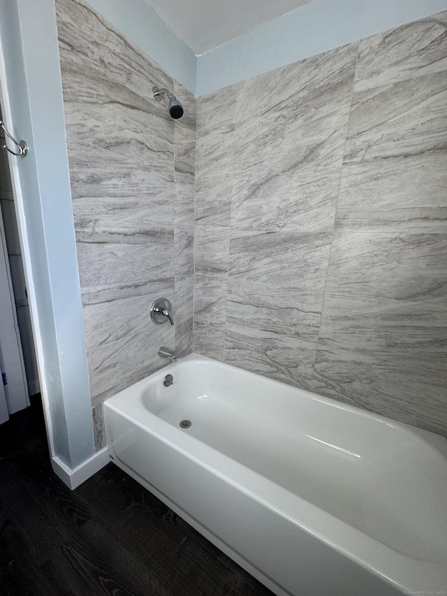 bathroom with washtub / shower combination, baseboards, and wood finished floors