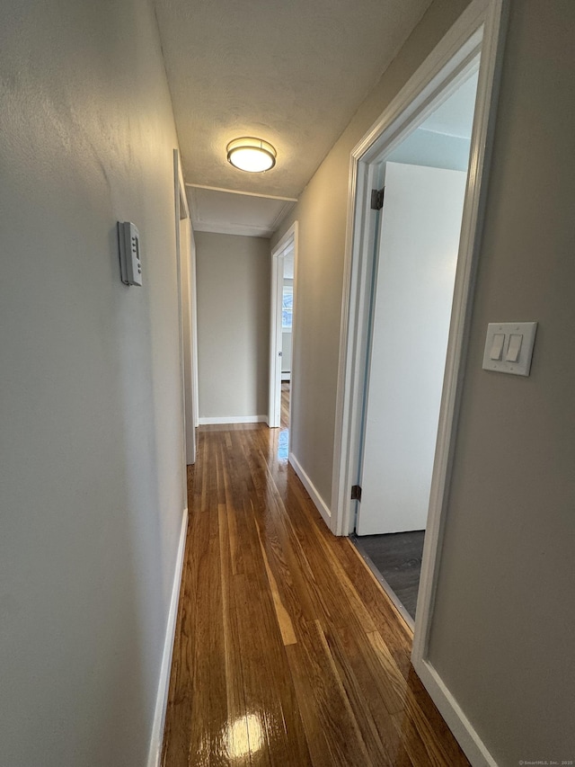 hall featuring baseboards, a textured ceiling, and wood finished floors