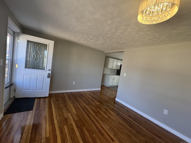 interior space with a notable chandelier, dark wood-style floors, baseboards, and a textured ceiling