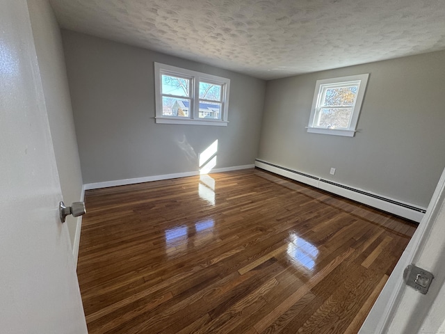 empty room featuring a textured ceiling, wood finished floors, baseboards, and a baseboard radiator