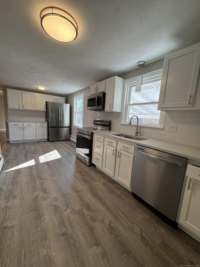 kitchen featuring dark wood finished floors, backsplash, appliances with stainless steel finishes, and a sink