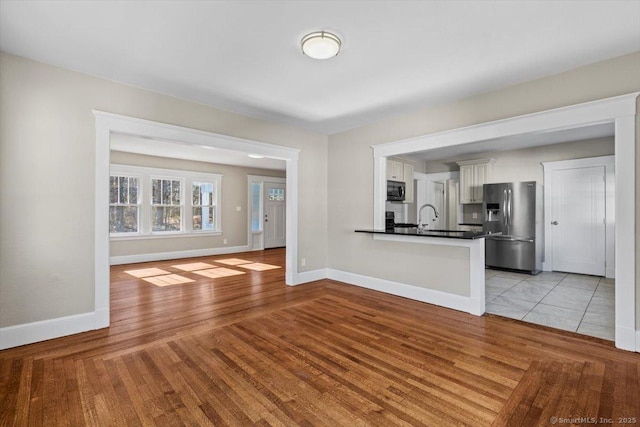 unfurnished living room featuring a sink, light wood-style flooring, and baseboards