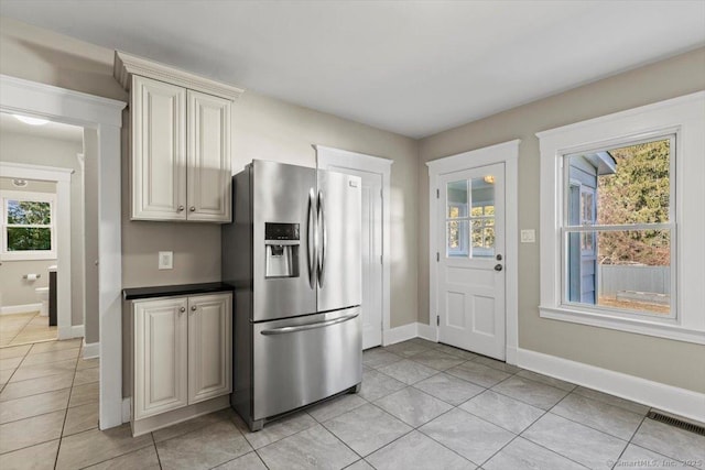 kitchen featuring light tile patterned floors, dark countertops, stainless steel fridge with ice dispenser, visible vents, and baseboards