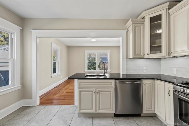 kitchen featuring stainless steel appliances, dark countertops, a healthy amount of sunlight, a sink, and a peninsula