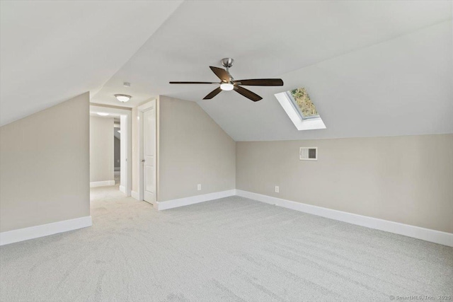 bonus room featuring vaulted ceiling with skylight, baseboards, visible vents, a ceiling fan, and light colored carpet