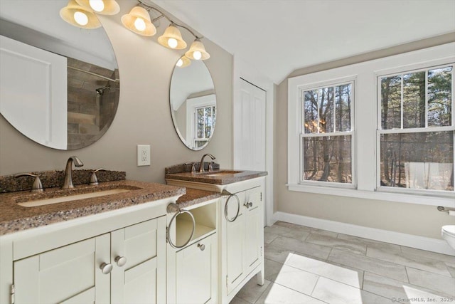 full bathroom with toilet, two vanities, a sink, and baseboards