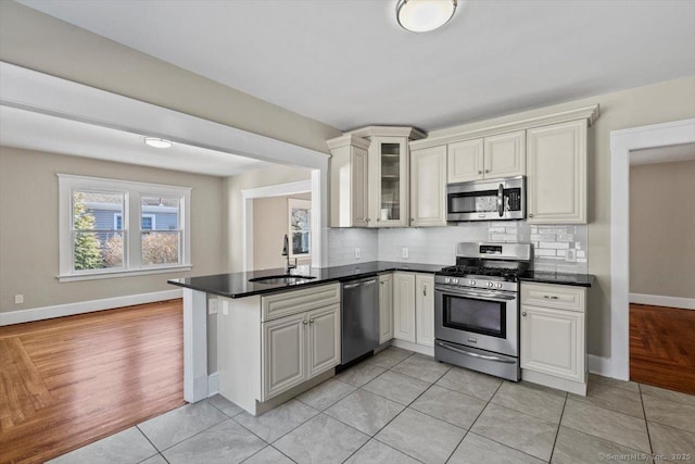 kitchen featuring stainless steel appliances, tasteful backsplash, a peninsula, and a sink