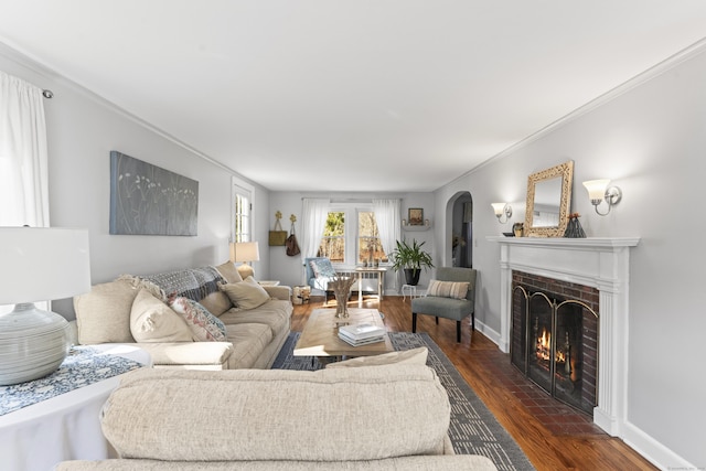 living room featuring a fireplace with flush hearth, arched walkways, crown molding, baseboards, and dark wood-style flooring