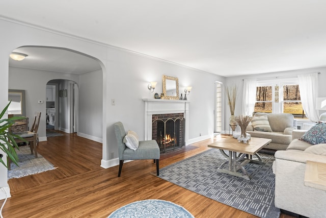 living room with arched walkways, a brick fireplace, baseboards, and wood finished floors