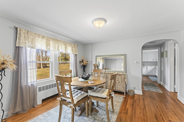 dining space featuring baseboards, arched walkways, wood finished floors, and radiator heating unit