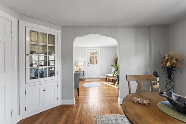 interior space featuring arched walkways, ornamental molding, baseboards, and hardwood / wood-style floors