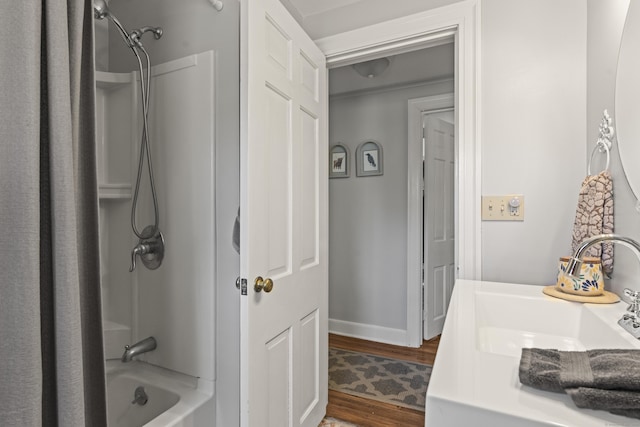 bathroom with a sink, baseboards, wood finished floors, and washtub / shower combination