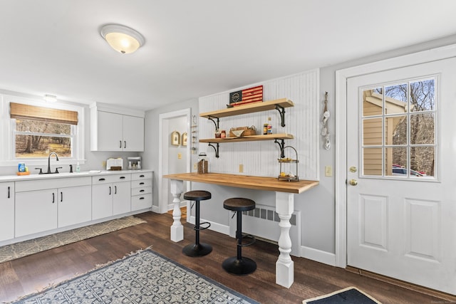 kitchen featuring baseboards, dark wood finished floors, open shelves, a sink, and white cabinets