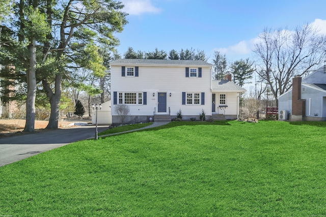 view of front of house featuring entry steps, driveway, a chimney, and a front lawn